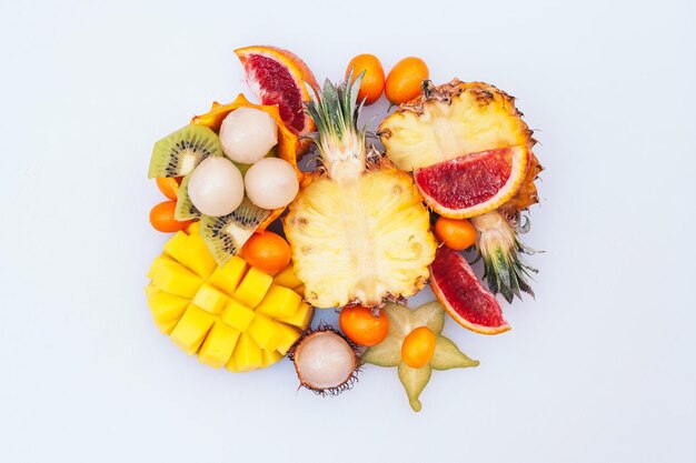 Photo assortment of tasty juicy exotic fruit on white background sliced mango rambutan mini pineapple starfruit healthy eating concept