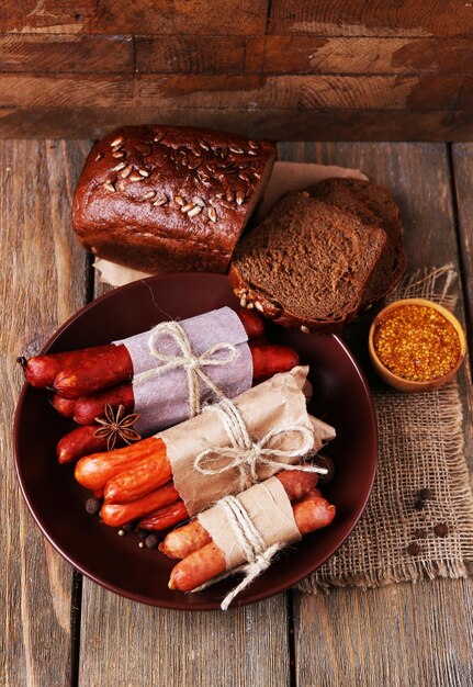 Assortment of thin sausages and spices on plate on wooden background