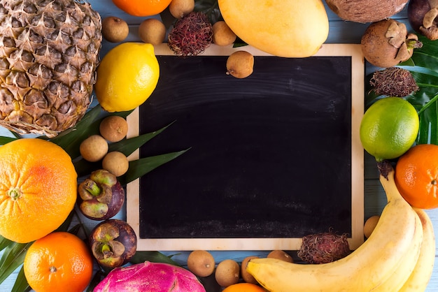 Assortment of tropical fruits with leaves of palm trees and and chalk board 