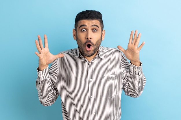 Astonished businessman standing with open mouth and raised arms being impressed of shocking news