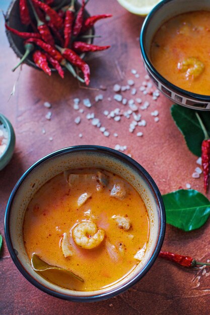 Asty asian soup tom yam in small bowls chilli pepper salt and coconut and lime on a dark brown background