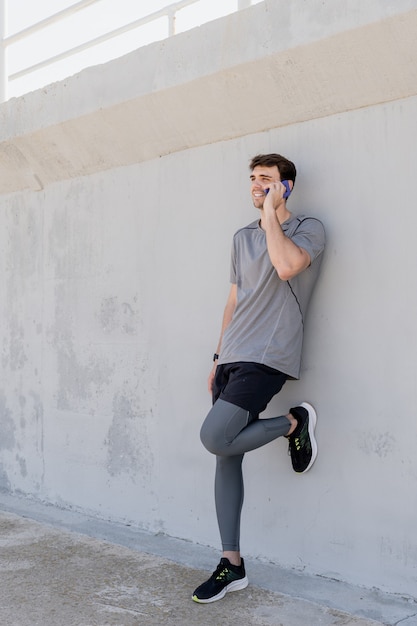 Athlete boy talking on the mobile leaning on the wall with a big smile