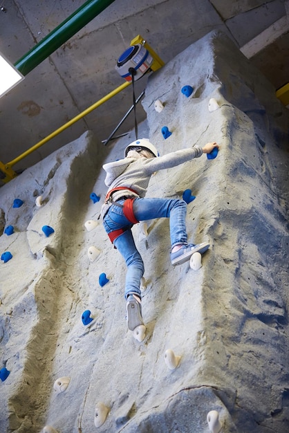 Athlete girl is climbing to amusement park on blue wall