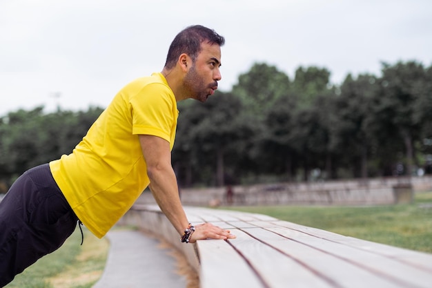 Athlete man builds arm muscles with bench pushups in park preparing for triumph on sports arena