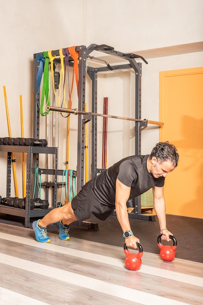 Athlete man doing excercise of push ups with kettlebell in gym. Concept of exercise with equipment in gym.