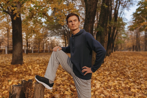 athlete stretching legs leaning on tree while having fitness training outdoors in autumn park