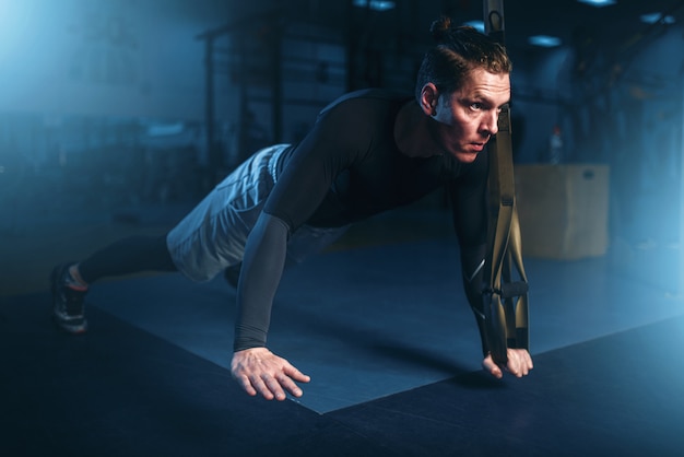 Athlete on training, pushup exercise with rope in gym.