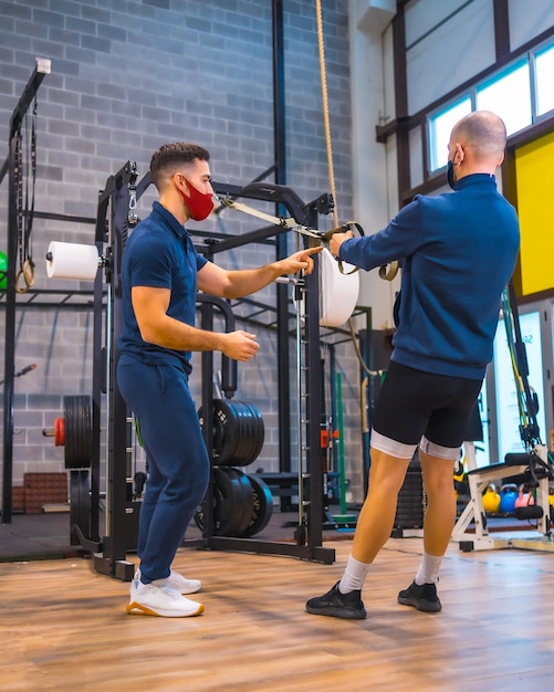 An athlete with an instructor in the gym doing arm exercises in the coronavirus pandemic a new normal With protective face mask