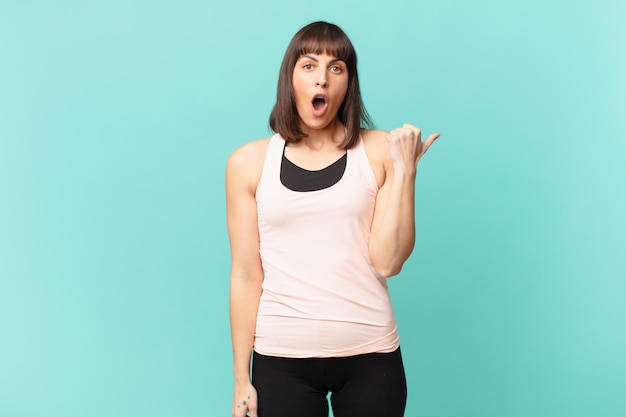 Athlete woman looking astonished in disbelief, pointing at object on the side and saying wow, unbelievable