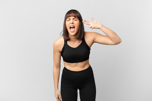 Athlete woman looking unhappy and stressed, suicide gesture making gun sign with hand, pointing to head