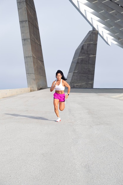 Athlete woman in sportswear running strong through the city front view