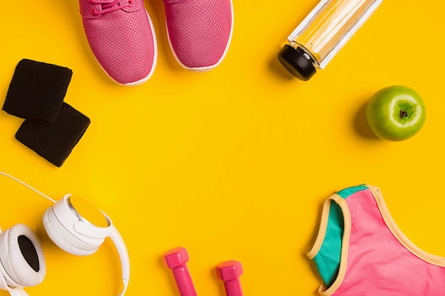 Athletes set with female clothing dumbbells and bottle of water on yellow background