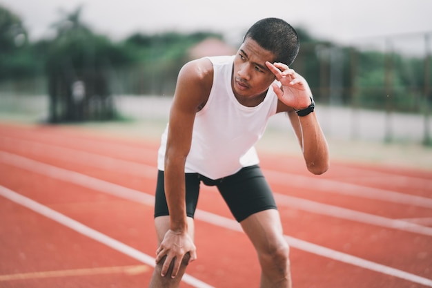 Athletes sport man runner wearing white sportswear tired wipe sweat and resting after practicing on a running track at a stadium Runner sport concept