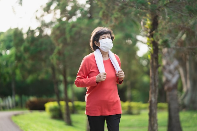 Athletic asian senior woman 60s wearing surgical mask to protect virus covid19 coronavirus or PM 25 Particulate Matters and jogging Senior asian woman running at the park on a dusty day