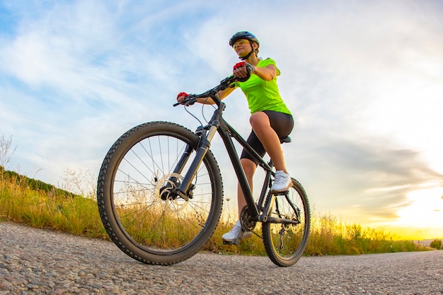 Athletic beautiful cyclist rides a bicycle on the road against the backdrop of nature