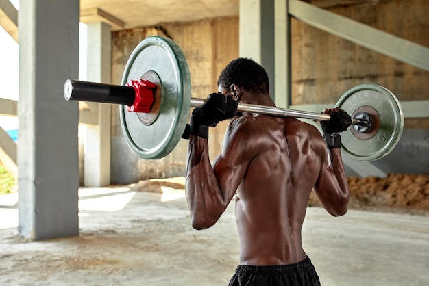 Athletic black young man lifting a heavyweight barbell in outdoor gym under the bridge Healthy lifestyle concept