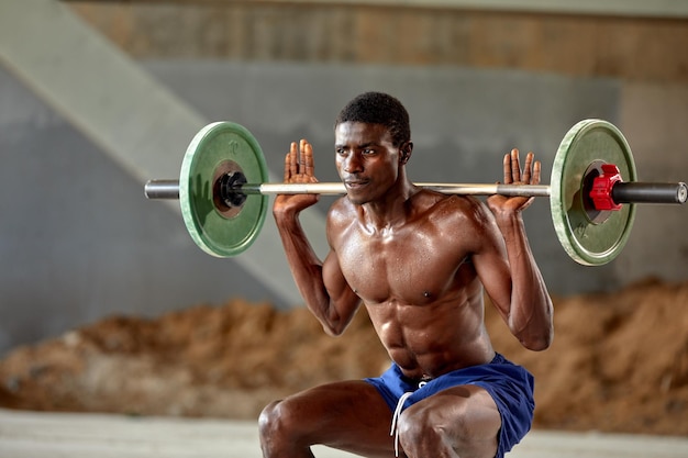 Athletic black young man lifting a heavyweight barbell in outdoor gym under the bridge Healthy lifestyle concept