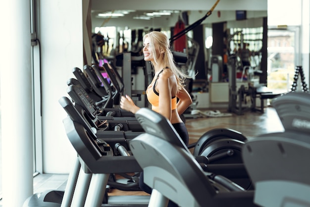 Photo athletic blond woman running on treadmill at gym