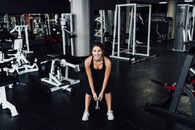 Athletic body, attractive girl in the gym with dumbbells in hand