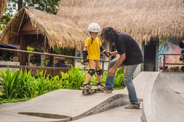 Athletic boy learns to skateboard with asian trainer in a skate park Children education sports Race diversity