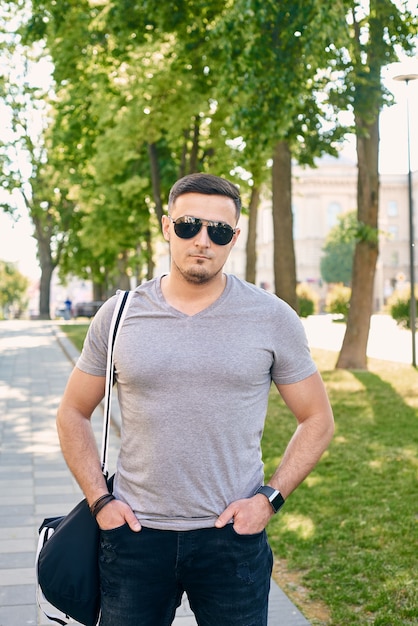 Athletic Caucasian man in a gray T-shirt with sunglasses stands against the background of trees