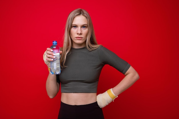 Athletic female boxer drinks water on red background