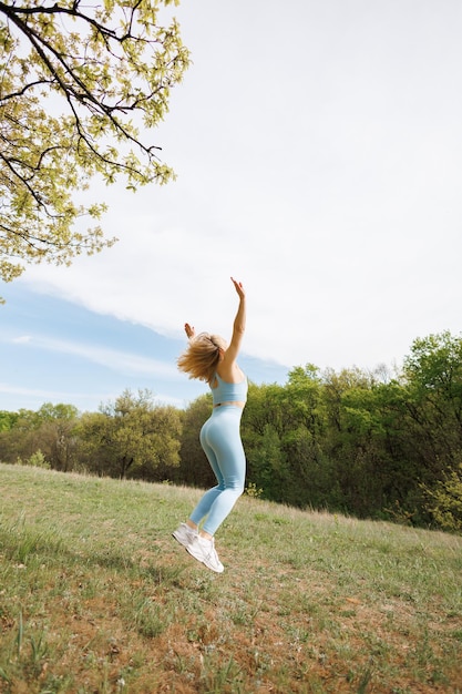 An athletic girl performs the exercise of jumping up with her arms raised Beautiful blonde