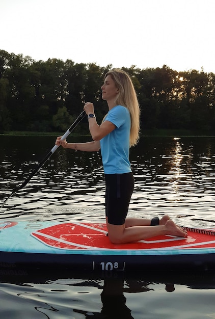 Athletic girl swims on a paddleboard for swimming SUP on her knees and rows with a paddle