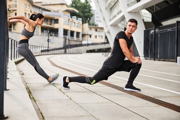 Athletic handsome man is doing lunges and slim woman is doing triceps push ups in urban street