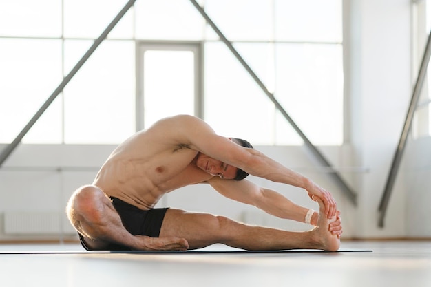 Athletic latin man doing yoga doing exercises while sitting in gym Concept of training in gym