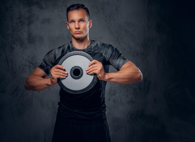 Athletic male holds a barbell weight in his arm over grey background.