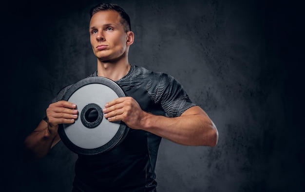 Athletic male holds a barbell weight in his arm over grey background.