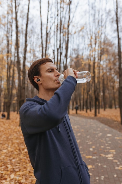 athletic male jogger drinking water from reusable water while taking break during training