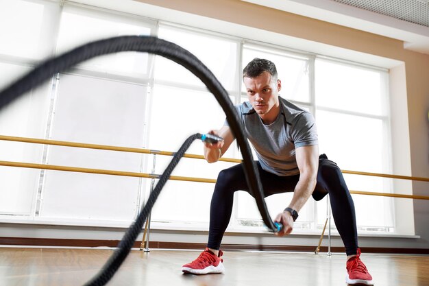 Athletic man doing rope exercise sneaker with ropes in the sports concept of the gym