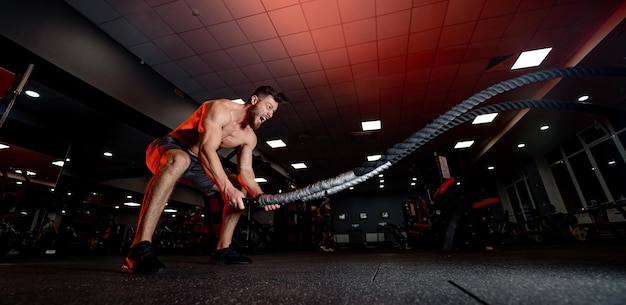 Athletic man doing some cross-training exercises with ropes in gym. Heavy training.