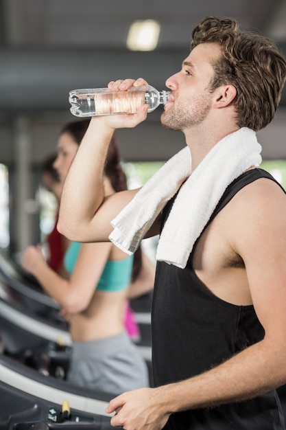 Athletic man drinking water while running on treadmill in gym