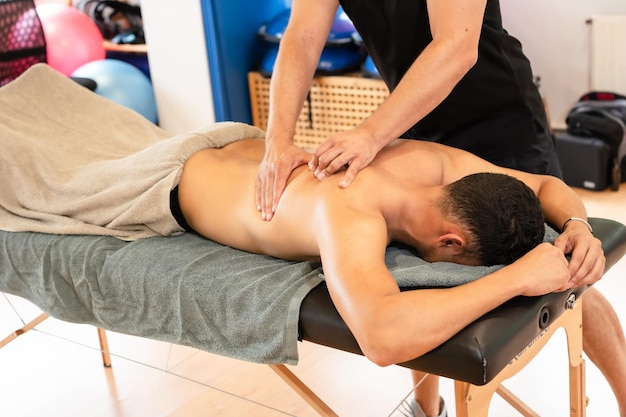 An athletic man receiving a recovery massage by a physiotherapist on a stretcher therapeutic back massage and osteopathy in the same sports center