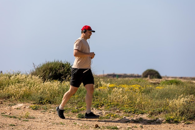 Athletic man running in park with headphones on sunny summer day Healthy lifestyle Active adult men is jogging