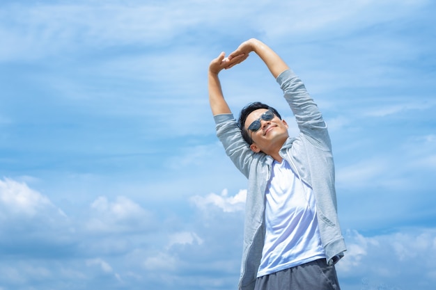 Athletic man stretching his arms up in the blue sky 