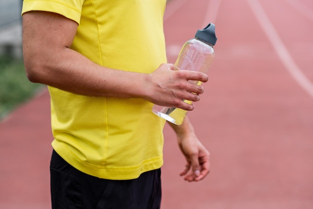 Athletic man in tracksuit holding transparent bottle of water standing on running track