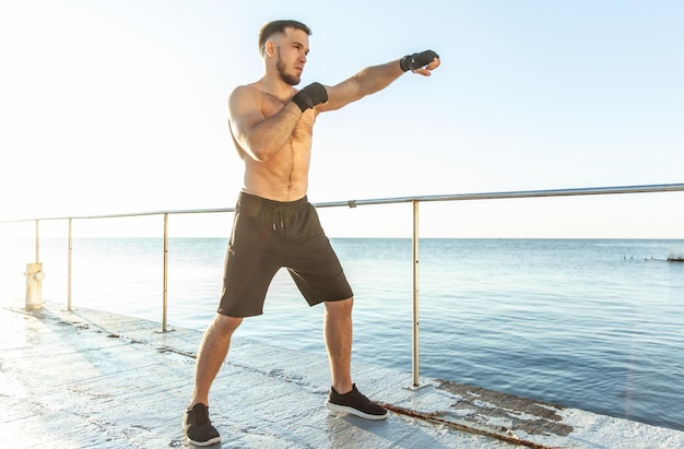 Athletic man training kicks in the early morning on the beach