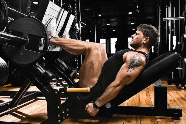 Athletic man trains legs on the simulator in the gym with weight. Athletic body, healthy lifestyle, fitness motivation, body positive.