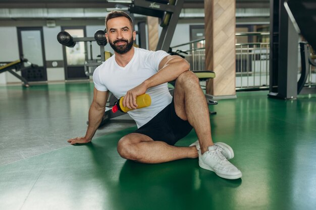 Athletic man in white tshirt relaxing on gym floor after training