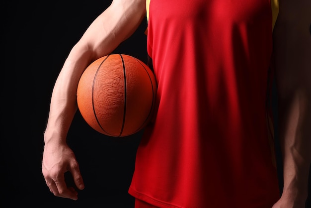 Athletic man with basketball ball on black background closeup