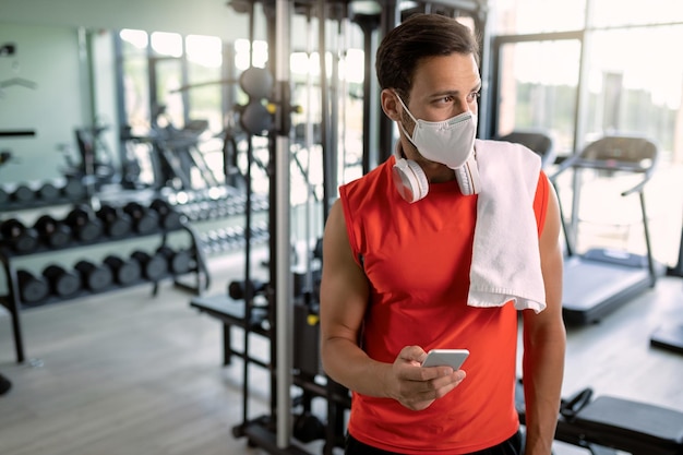 Athletic man with face mask texting on mobile phone in a gym