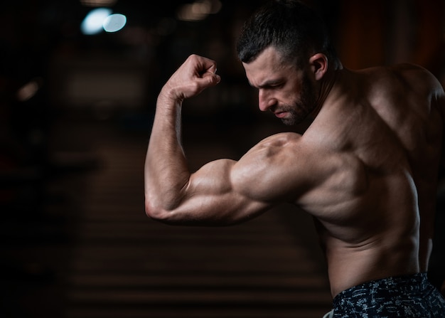 Athletic man with a muscular body poses in the gym, showing off his biceps