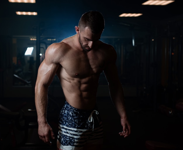 Athletic man with a muscular body poses in the gym, showing off his muscles