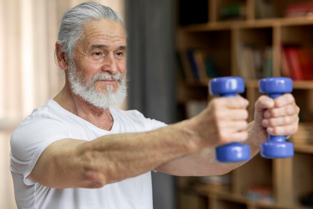 Athletic old man exercising at home using blue barbells