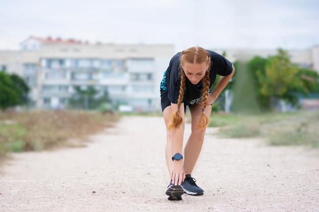 Athletic redhaired woman warming up before training stretches outdoors alone in summer