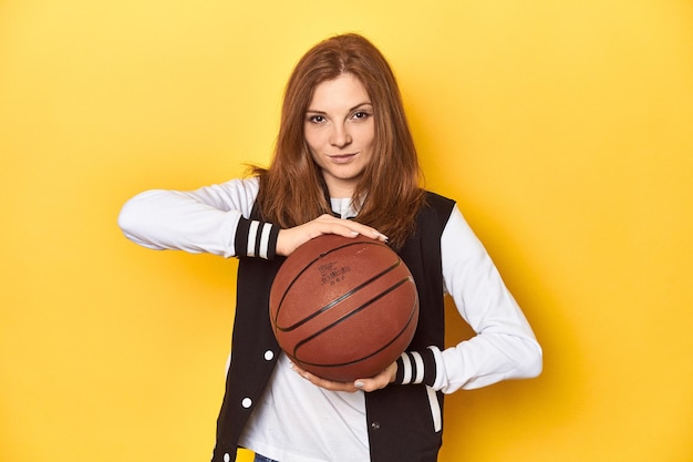 Athletic redhead woman with basketball yellow studio background